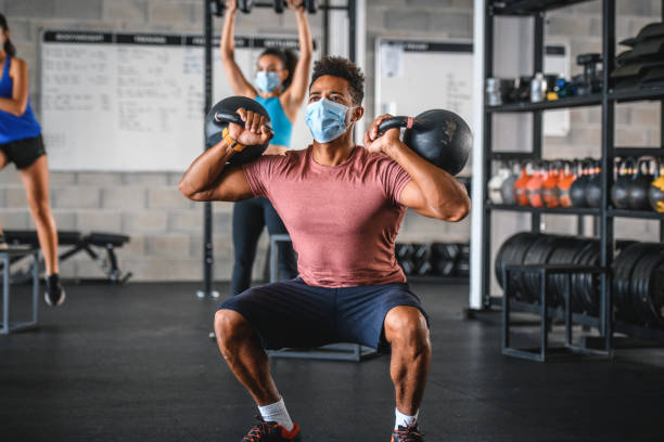 istock Masked Black Athlete Doing 2-Kettlebell Front Squat in Gym 1279440676