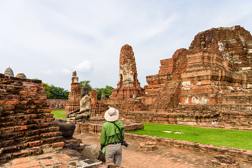A tourist man admiring the old ruin at Wat Phra Mahathat, Ayutthaya Historical Park, Thailand Raining Season