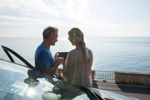 couples matures se détendre à côté de la porte de voiture, regarder la tablette numérique - car door flash photos et images de collection