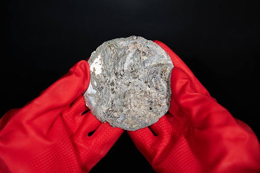 A man in thick gloves holds a metal button that looks like a plutonium button.