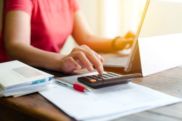 istock Female punches number in a calculator while using a laptop - Paying Bills - Desk 1279449460