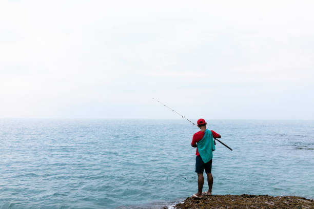asian man wearing hat fishing on the beach