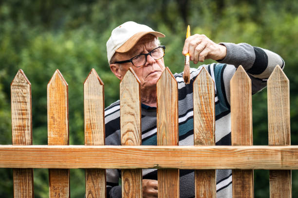 Senior man painting wooden fence in garden Renovation of old wooden picket fence. Domestic life and work in retirement. Old man paint wood stain fence3 stock pictures, royalty-free photos & images
