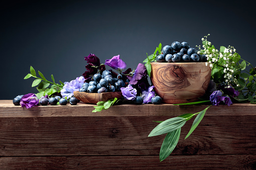 Fresh juicy blueberries in wooden bowl. Summer still life with blueberries, colored sweet peas and meadow grasses on an old wooden table. Copy space.