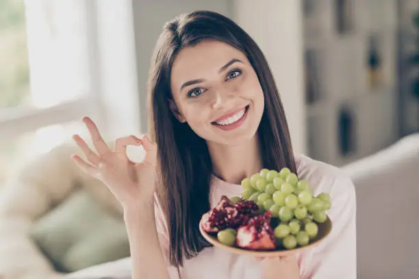 Close-up portrait of her, she nice attractive charming cheerful cheery brown-haired girl holding in hands fresh berries showing ok-sign advice advert ad fitness life staying home apartment