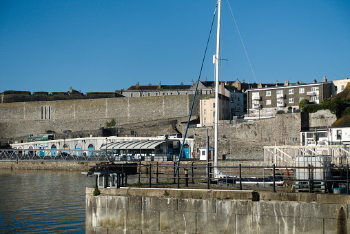 Plymouth England. The walls of the Royal Citadel as seen across the water of Sutton harbour. Boats on the calm water with blue sky
