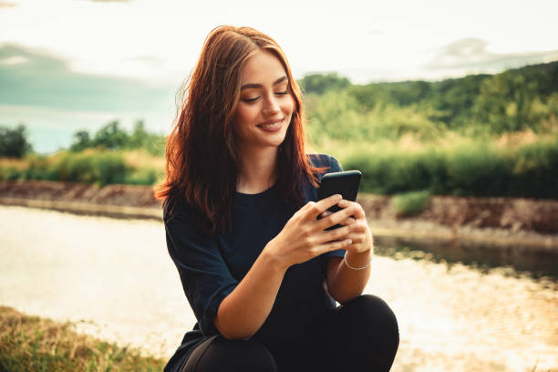 彼女のスマートフォンにメッセージを書く幸せな笑顔の若い女性 - nature smiling teenage girls female ストックフォトと画像