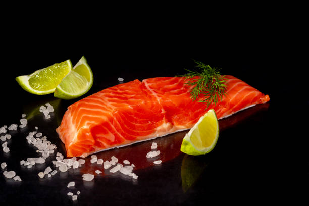 istock Lightly salted trout. Fresh fish fillet with culinary ingredients, herbs and lemon on a black background, side view. 1279481059