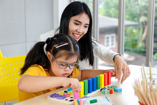 Asian girl with Down's syndrome play puzzle toy with her teacher in classroom.