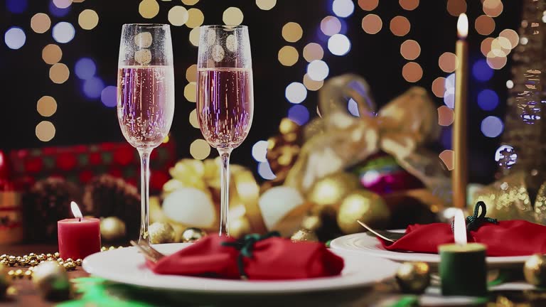 Dolly shot of Champagne flutes in table for two over golden holiday background. Christmas and New Year celebration
