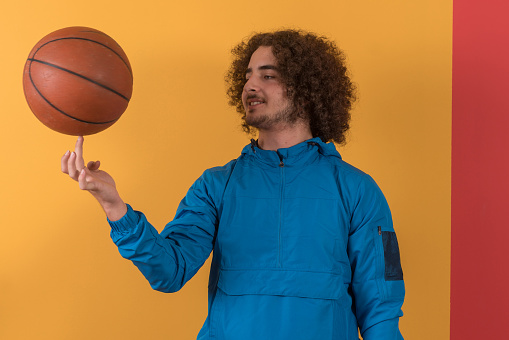 Handsome young man playing a basketball ball  in front of colored wall.