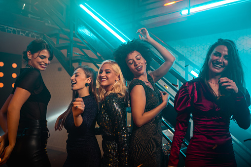 Group of young female friends dancing together in the nightclub surrounded by confetti