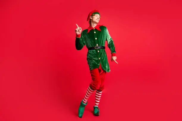 Full length photo of handsome x-mas north-pole jolly elf dance wear x-mas costume isolated red bright color background.