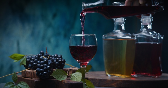 Pouring red wine against blue background with red grapes and wine bottles