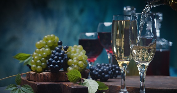 Pouring white wine against blue background with red and white grapes and wine bottles