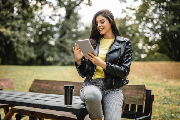 joven mujer hermosa bebiendo café y leyendo e-book en tableta digital al aire libre - reading newspaper break tea fotografías e imágenes de stock