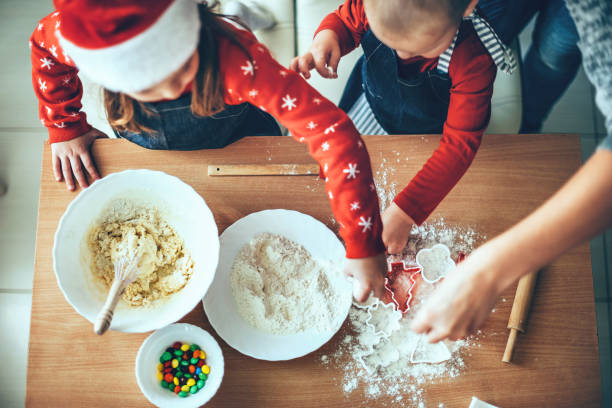 obere ansicht foto von kindern, die kekse mit mehl und teig für weihnachten tragen santa kleidung - baking lifestyles beautiful cookie stock-fotos und bilder