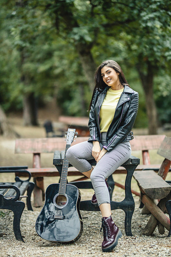 Portrait of beautiful young female artist with her black acoustic guitar at the park