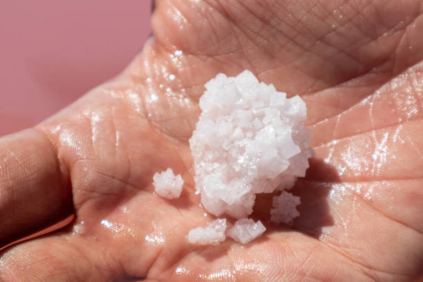 istock Hand holding salt crystal near pink water surface 1279513962