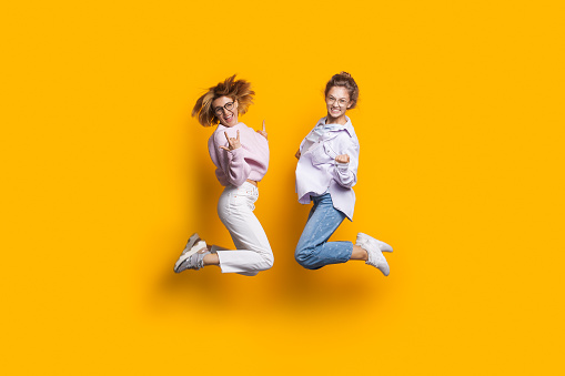 Dos hermanas rubias saltando en una pared de estudio amarillo y sonríen a la cámara gesturing felicidad photo