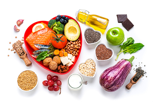 Healthy eating: group of fresh multicolored foods to help lower cholesterol levels and for heart care shot on white background. The composition includes oily fish like salmon and sardines. Beans like Pinto beans and brown lentils. Vegetables like garlic, avocado, broccoli, eggplant and tomatoes. Fruits like apple, grape, orange and berries. Nuts like almonds and walnuts. Soy products like tofu and soy milk. Cereals and seeds like chia seeds, flax seeds, oatmeal and barley. Olive oil and yogurt with added sterols and stanols. High resolution 42Mp studio digital capture taken with SONY A7rII and Zeiss Batis 40mm F2.0 CF lens