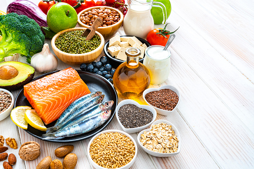 Healthy eating: group of fresh multicolored foods to help lower cholesterol levels shot on wooden table. The composition includes oily fish like salmon and sardines. Beans like Pinto beans and brown lentils. Vegetables like garlic, avocado, broccoli, eggplant and tomatoes. Fruits like apple, grape, orange and berries. Nuts like almonds and walnuts. Soy products like tofu and soy milk. Cereals and seeds like chia seeds, flax seeds, oatmeal and barley. Olive oil and yogurt with added sterols and stanols. High resolution 42Mp studio digital capture taken with SONY A7rII and Zeiss Batis 40mm F2.0 CF lens