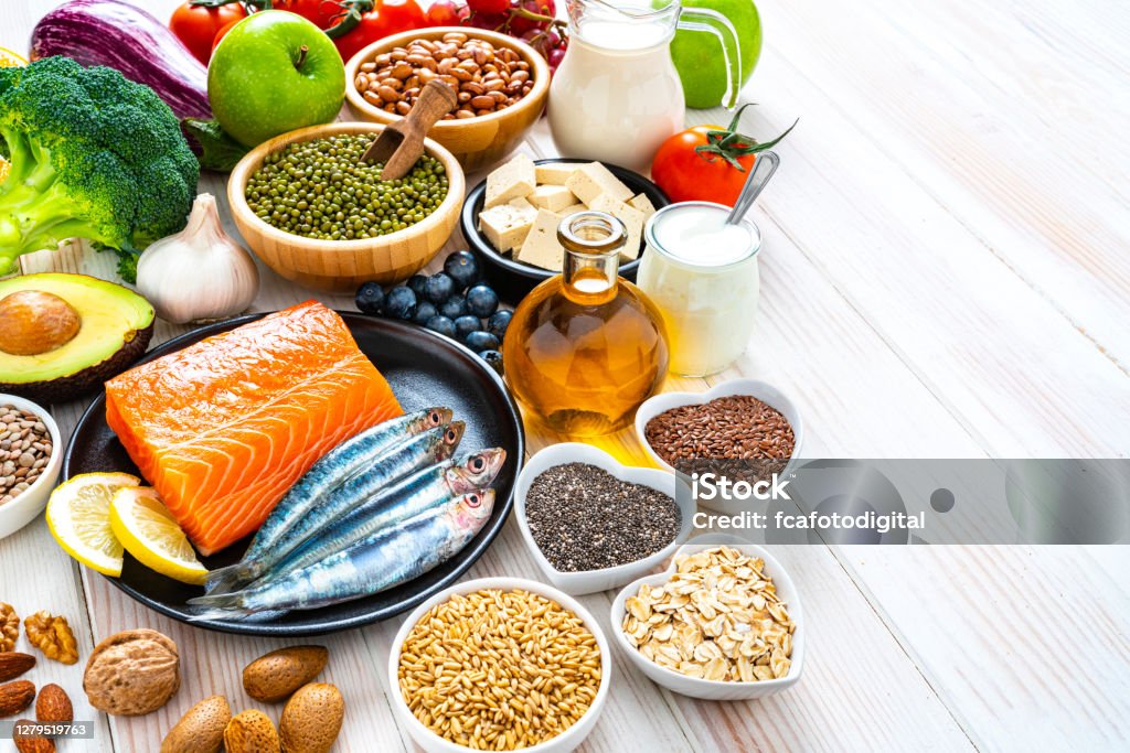 Foods to lower cholesterol and heart care shot on wooden table. Copy space Healthy eating: group of fresh multicolored foods to help lower cholesterol levels shot on wooden table. The composition includes oily fish like salmon and sardines. Beans like Pinto beans and brown lentils. Vegetables like garlic, avocado, broccoli, eggplant and tomatoes. Fruits like apple, grape, orange and berries. Nuts like almonds and walnuts. Soy products like tofu and soy milk. Cereals and seeds like chia seeds, flax seeds, oatmeal and barley. Olive oil and yogurt with added sterols and stanols. High resolution 42Mp studio digital capture taken with SONY A7rII and Zeiss Batis 40mm F2.0 CF lens Healthy Eating Stock Photo