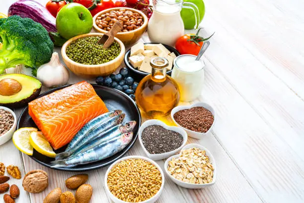 Healthy eating: group of fresh multicolored foods to help lower cholesterol levels shot on wooden table. The composition includes oily fish like salmon and sardines. Beans like Pinto beans and brown lentils. Vegetables like garlic, avocado, broccoli, eggplant and tomatoes. Fruits like apple, grape, orange and berries. Nuts like almonds and walnuts. Soy products like tofu and soy milk. Cereals and seeds like chia seeds, flax seeds, oatmeal and barley. Olive oil and yogurt with added sterols and stanols. High resolution 42Mp studio digital capture taken with SONY A7rII and Zeiss Batis 40mm F2.0 CF lens