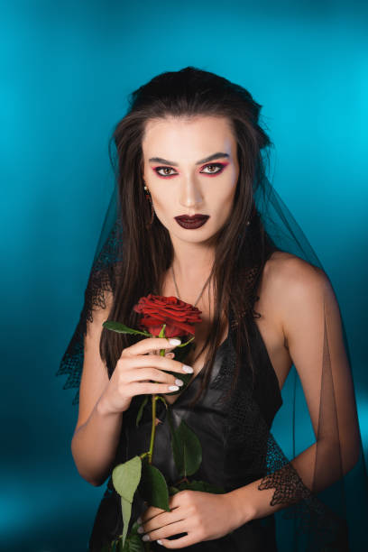 young brunette woman with dark makeup holding red rose on blue