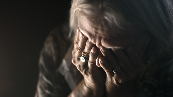 Desperate senior crying in a dark room. Perfectly usable for a wide range of topics like depression, loneliness or mental health in general.