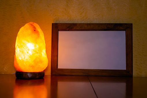 Glowing electric salt lamp on a wooden table with a photo frame in which you can write your text.