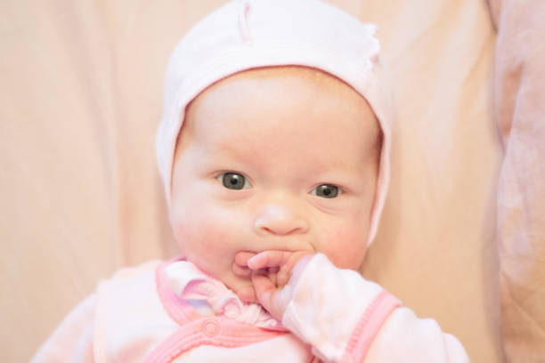 istock A baby in a pink cap is sucking his hand. 1279537266