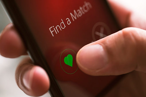 Online dating app on smart phone screen, close up. Hand touching like button with heart shape.