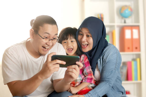 Happy muslim family looking at smart phone together, mother father and baby girl daughter playing games or doing video call at home Happy muslim family looking at smart phone together, mother father and baby girl daughter playing games or doing video call at home, smiling faces happy malay couple stock pictures, royalty-free photos & images