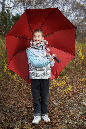 Girl in warm clothes posing with an umbrella in an autumn park
