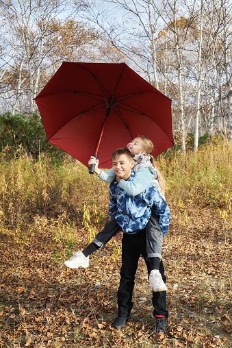 A boy rolls a girl with an umbrella on his back while walking in the autumn park