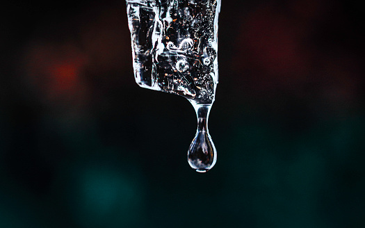 Macro close up of ice melting and a droplet of water about to fall from it with a dark blurred background