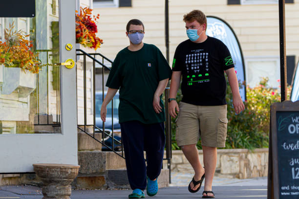Two young men both wearing face masks due to COVID-19 are walking in the street. Ellicott City, MD, USA 10/07/2020: Two young men both wearing face masks due to COVID-19 are walking in the street. They have casual summer outfit. Concept image for Social life during pandemic ellicott city maryland stock pictures, royalty-free photos & images