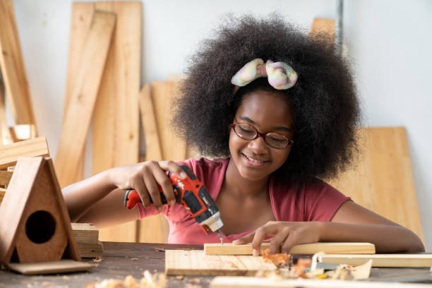 A little African American inventor practice to be a carpenter in carpentry shop A little African American inventor practice to be a carpenter in carpentry shop. A girl working as woodworker to drill holes in a wooden plank at workshop. DIY woodworking crafts and Hobbies concepts carpenter carpentry craftsperson carving stock pictures, royalty-free photos & images