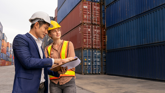 Businessmen consult with engineer about transport container in shipping yard. Inspector talking with dock worker and used clipboard checking cargo freight. Concept of logistics and transportation.