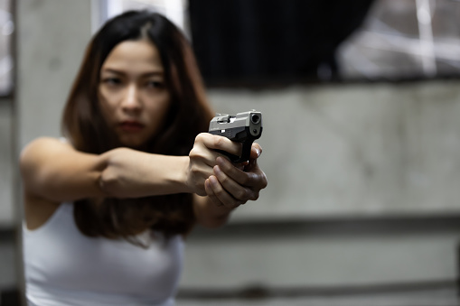 Woman aiming a gun at abandoned house background. With focus on the gun