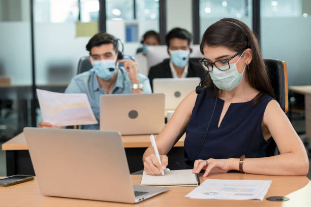 Female operator wears surgical masks to prevent pandemic of the covid-19 coronavirus in a call center Female operator wears surgical masks to prevent pandemic of the covid-19 coronavirus in a call center. Telemarketer used headset answering customer questions. Security measures of new normal life covid secure photos stock pictures, royalty-free photos & images