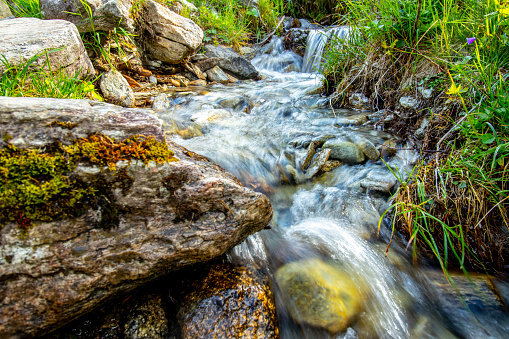 A small stream of fresh glacier water flowing over rocks in cascades with grass on the sides in Hintertux, Austria.