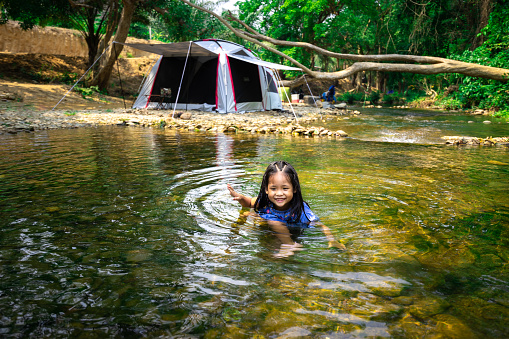 Portrait of little asian girl playing nature water near tent while going camping in nature park