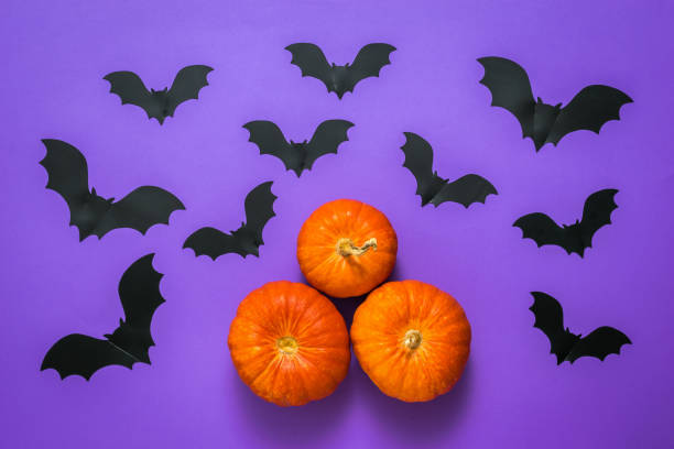 istock Three pumpkins and a large number of bats on a lilac background. 1279582157