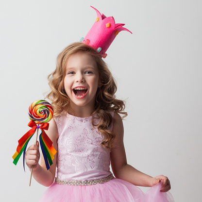 Beautiful excited candy princess girl in crown holding big lollipop and screaming of joy