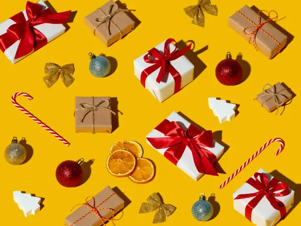 Yellow Christmas background. Holiday gift pattern. New Year care package. Colorful festive composition. Rustic beige white boxes with red ribbon bows ball candy cane ornament isolated on orange.