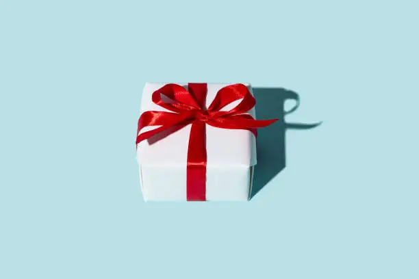 Birthday gift. Holiday surprise. Care package. Special day greeting. Present wrapped in white box with red ribbon bow isolated on blue copy space background.