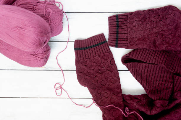 istock maroon knitted sweater with pattern and balls of wool threads next to it on light wooden background. Knitting lessons online 1279594392