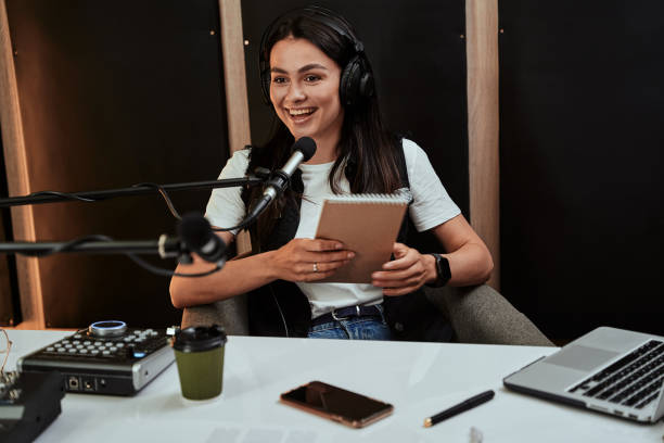 portait de atraente jovem apresentadora de rádio segurando um roteiro, olhando emocional enquanto fala no microfone, moderando um show ao vivo - locutor de radio - fotografias e filmes do acervo